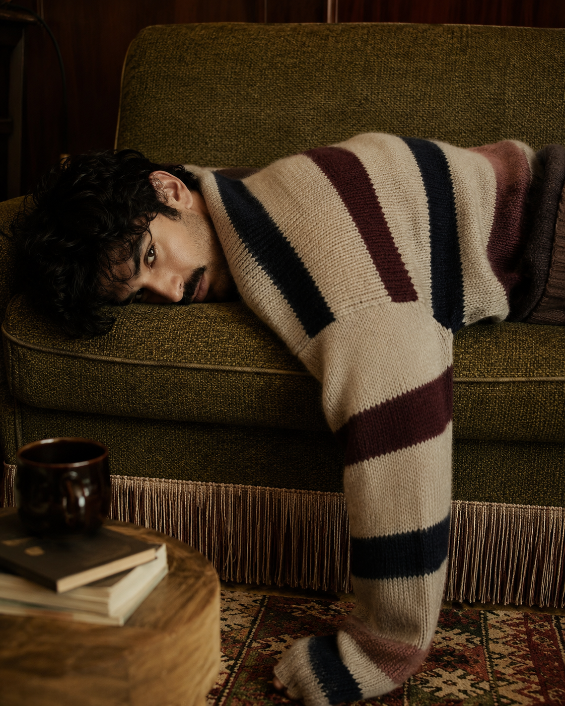 Man draped over a green couch in a striped knit sweater