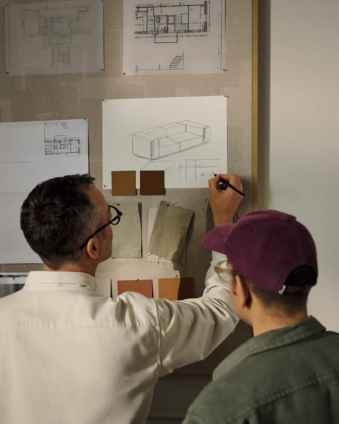 Architects marking up a sketch pinned beside leather and linen samples