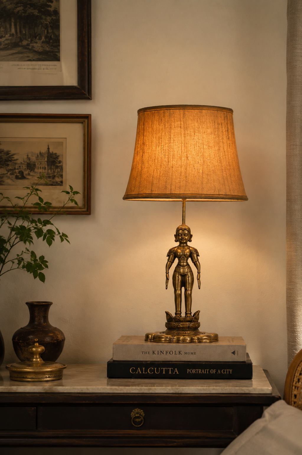 Brass figure lamp on a marble console beside framed etchings